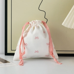 Detail of a beige drawstring bag with pink bow patterns and braided cords in a home setting