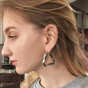 Model wearing large silver triangle stud earrings with a polished geometric finish