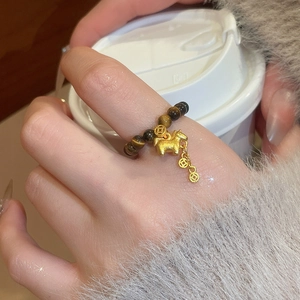 Macro shot of tiger eye bead ring with golden horse and ancient coin charms on finger