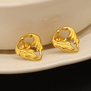 Close-up of golden hollow feather earrings resting on a white ceramic plate