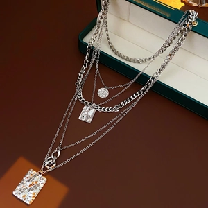 Detail of silver layered necklace with hammered square pendants draped over a green jewelry box