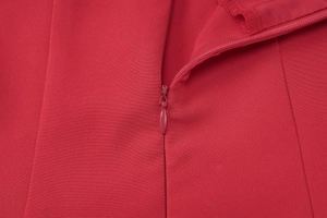 Detail shot of the hidden zipper on the back of a red V-neck dress with fabric texture
