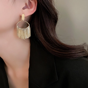 Close-up of elegant gold tassel oval earrings worn by a model in a black suit
