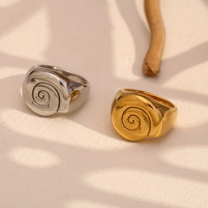 Detail of spiral signet rings in gold and silver finish on warm textured background