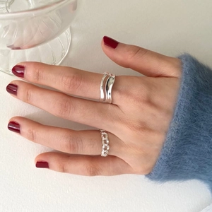 Close-up of minimalist silver chain and irregular wavy rings on model finger