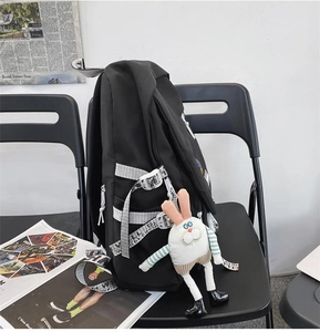 Detail of black canvas backpack with contrast lettering straps and white plush rabbit charm