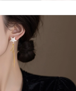 Detail of star-shaped earrings with gold tassels and zircon stones worn by a model