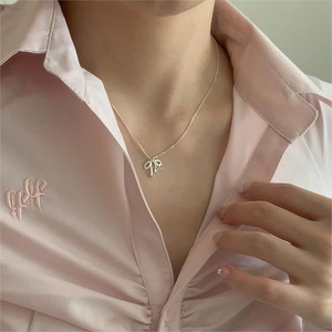 Close-up of S925 sterling silver bow pendant necklace worn by a model in a pink shirt