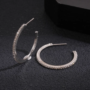 Macro shot of silver C-shaped hoop earrings with sparkling cubic zirconia on dark background