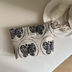 Detailed close-up of a cotton linen cosmetic bag with black butterfly embroidery and label