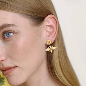 Boucles d'oreilles abeille et marguerite dorées avec zircon rouge portées par modèle