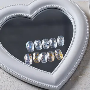 Macro shot of 10 clear press-on nails with holographic heart sequins and gold foil