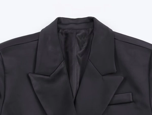 Detailed close-up of a black herringbone wool blazer showing lapel and pocket texture