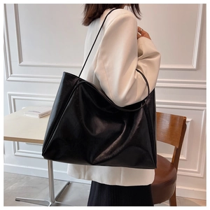 Detail of a large black tote bag on a white suit showing the smooth faux leather texture