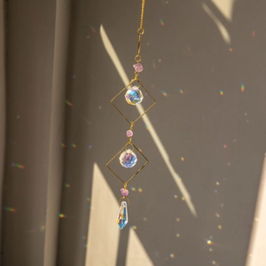 Hanging amethyst suncatcher with golden prisms creating rainbow light on a white wall