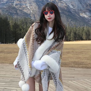 Detail of ethnic knit shawl featuring wave patterns and white faux fur trim with pom-poms