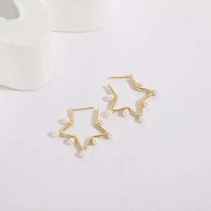 Minimalist gold star pearl earrings with white pearls on a geometric display stand