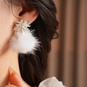 Detail shot of a silver snowflake earring with a soft white pompom on a model