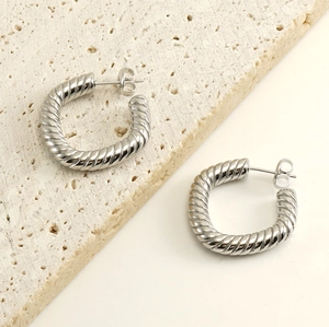 Macro detail of twisted silver hoop earrings with butterfly backs on stone display