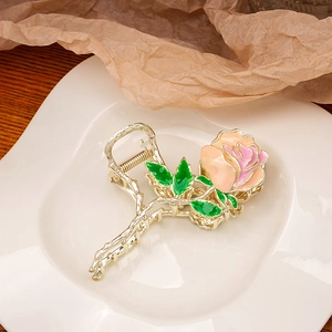 Detail of rose hair claw clip in gold metal with pink enamel petals and green leaf accents