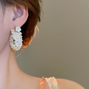 Detailed close-up of white floral cluster C-shaped earrings with gold bead accents