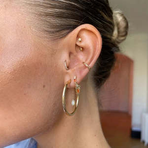 Macro detail of gold S925 sterling silver ear cuff set with orange zircon and tassel chain