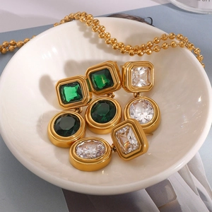 Gold-plated earrings and necklaces set with emerald and zircon stones in a ceramic bowl