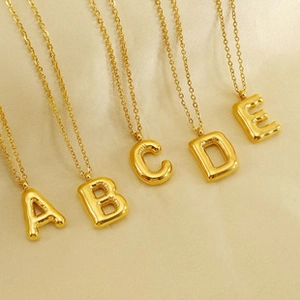 Detail of five 18K gold-plated initial necklaces on beige silk background