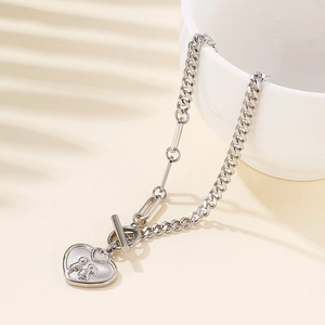 Silver Cuban link toggle bracelet with heart pendant and silhouettes on beige background