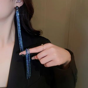 Close-up of long blue rhinestone fringe earrings worn by a model in a black suit