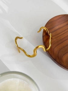 Detailed close-up of golden wavy cuff bracelet with polished mirror finish on white desk