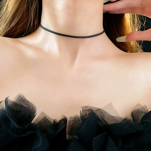 Close-up of a minimalist black leather choker necklace worn by a model on a dark background