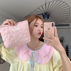 Detail of pink quilted floral cosmetic bag held by a person in a mirror selfie