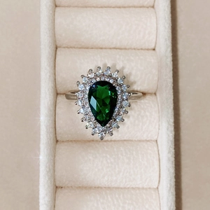 Macro di un anello a goccia di lusso con pietra verde e halo su velluto