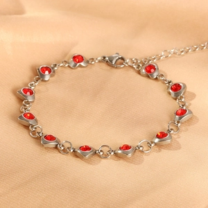 Close-up of heart-shaped silver bracelet with red zircon stones on silk background