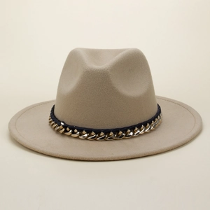 Close-up detail of beige fedora hat featuring gold chain and navy blue ribbon band