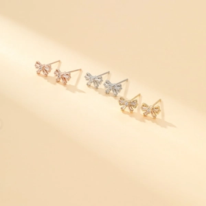 Detailed view of three bow-shaped stud earrings in gold, silver, and rose gold finishes