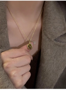 Detail of vintage gold necklace with oval tiger eye stone pendant on wool coat
