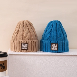 Close-up of thick cable knit winter hats with cute bear leather patch and Lucky text
