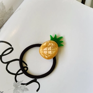 Detailed view of handmade pineapple charm hair tie with yellow finish and green leaves