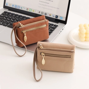 Detailed view of brown and beige pebble leather wallets with leaf zipper pulls and wrist straps