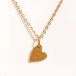 Gros plan du collier avec pendentif cœur doré gravé de la lettre O sur fond blanc épuré