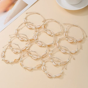 Flat lay of 12 bohemian shell and starfish braided bracelets set on a beige background