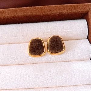 Macro view of gold-trimmed dark brown flocked geometric stud earrings on fabric