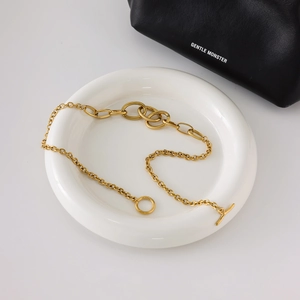 Detail of gold interlocking chain necklace with T-bar toggle clasp on ceramic plate