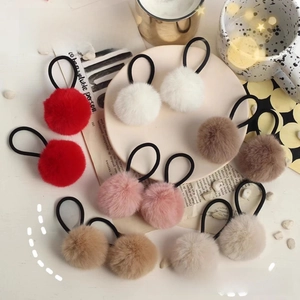 Close-up of assorted plush pom-pom hair ties in warm winter colors on a rustic tabletop