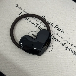Detail of a handmade black heart-shaped hair tie with golden logo on beige fabric