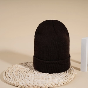 Close-up of deep brown cuffed beanie showing dense ribbed knit texture on woven mat