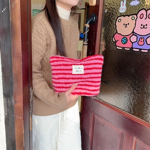 Close-up of a pink striped plush makeup bag held by a hand in a lifestyle setting