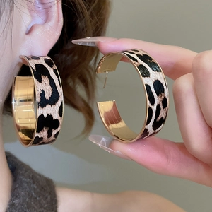 Close-up of gold C-shaped earrings with textured leopard print leather inlays for women